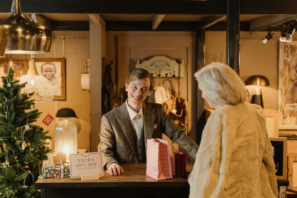 A cheerful shopkeeper assists a customer during a festive sale event in a cozy store setting.