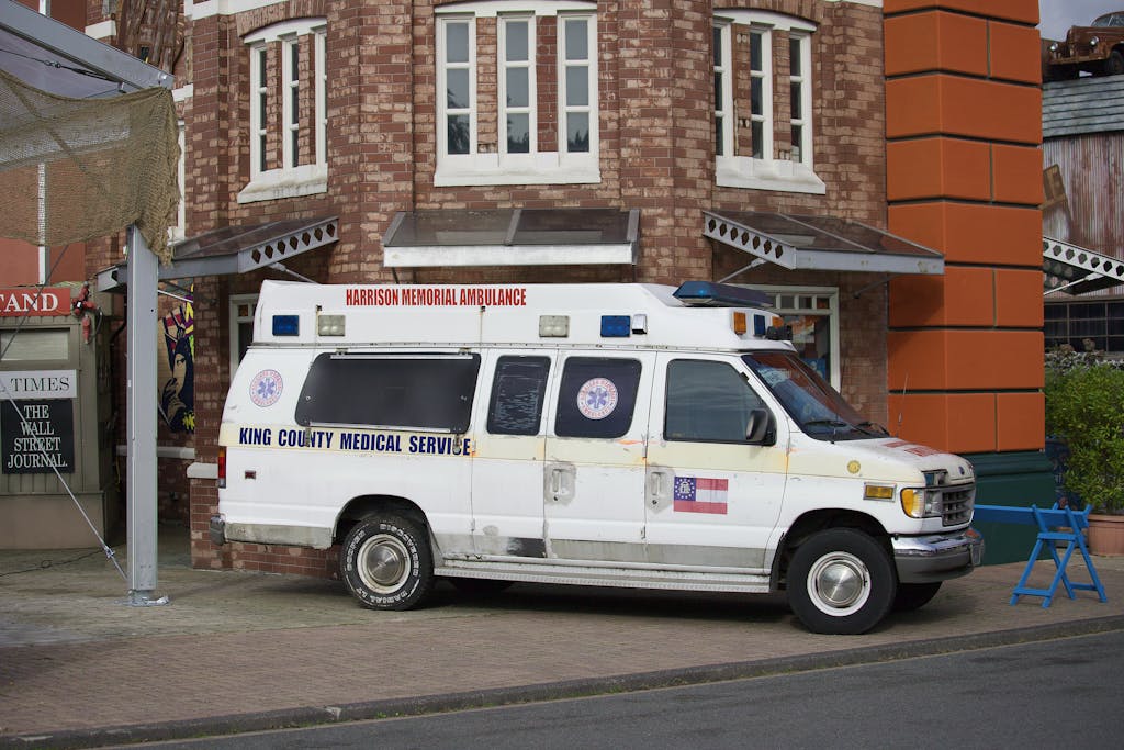 Old King County Medical Service ambulance parked beside a brick building on a street corner.