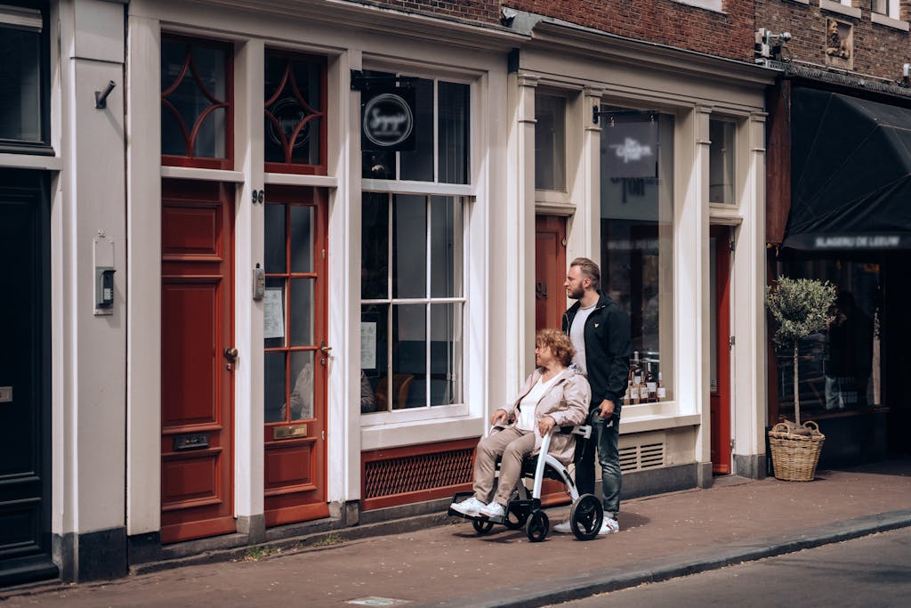 A man helps a woman in a wheelchair along a picturesque street in Amsterdam, Netherlands.